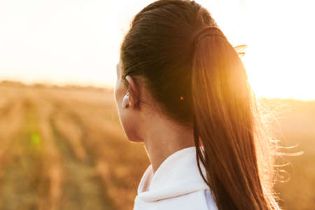 Image of adult brunette sportswoman using earphones while working out at golden fieldの写真素材