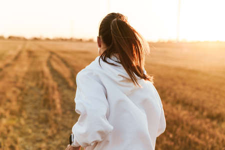 Image from back of adult beautiful sportswoman running while working out at golden fieldの写真素材