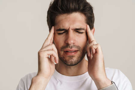 Image of unhappy young man with headache rubbing his temples isolated by white background