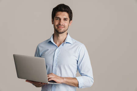 Image of smiling businesslike brunette man working with laptop isolated by beige backgroundの写真素材