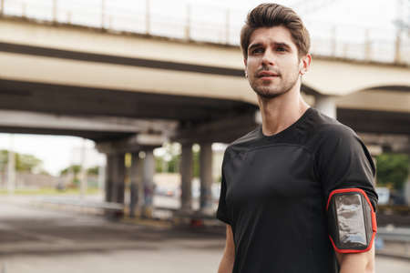 Image of athletic young sportsman with smartphone working out on city street