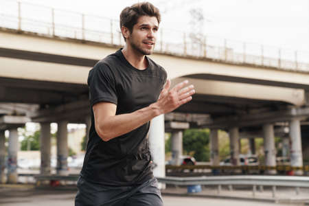 Image of athletic young sportsman running while working out on city street