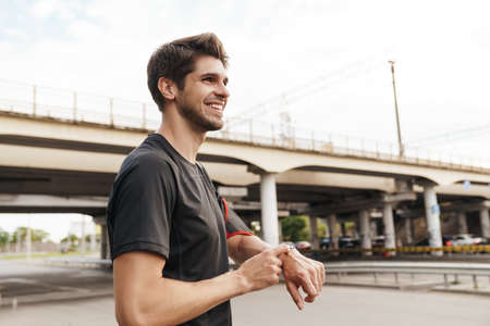Image of athletic smiling sportsman using smartwatch while working out on city street