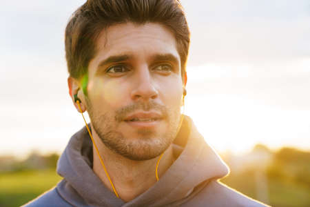 Image of athletic bristle sportsman using earphones and looking aside outdoors