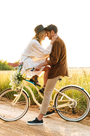 Image of young caucasian couple kissing while riding bicycle together in countryside