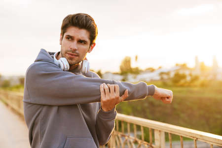 Image of athletic sportsman with headphones doing exercise while working out on city bridgeの写真素材