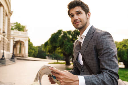 Image of a handsome pleased business man outdoors in park holding newspaper while looking asideの写真素材