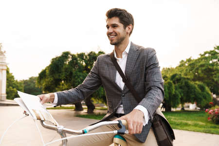 Image of a handsome happy cheerful business man outdoors in park on a bicycle looking asideの写真素材