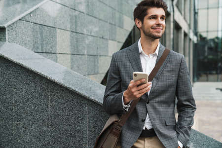 Image of happy handsome business man outdoors using mobile phone near business centerの写真素材