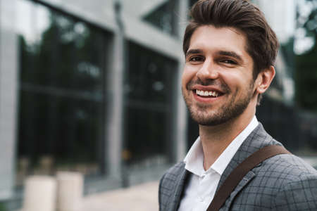 Image of cheerful smiling handsome business man outdoors near business center