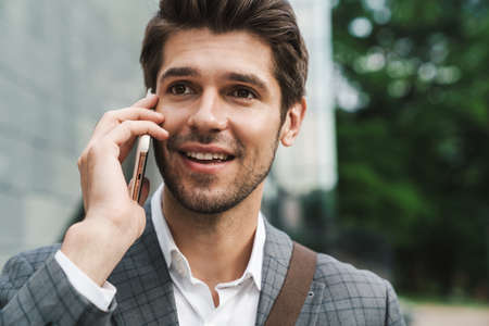 Image of happy cheerful business man outdoors talking by mobile phoneの写真素材