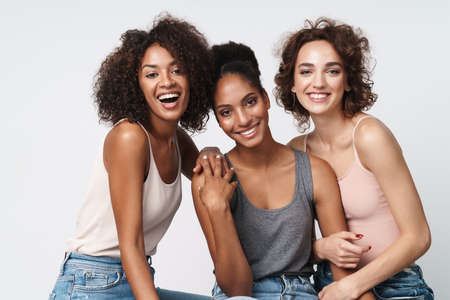 Portrait of three gorgeous multiracial women standing together and smiling at camera isolated over white backgroundの写真素材