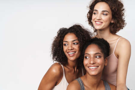 Portrait of three cheerful multiracial women smiling and looking aside isolated over white backgroundの写真素材