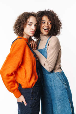 Portrait of nice multinational women in overalls looking at camera and hugging isolated over white backgroundの写真素材