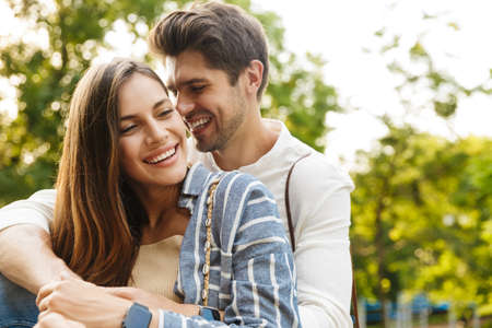 Image of young caucasian happy brunette couple smiling and hugging while walking in park