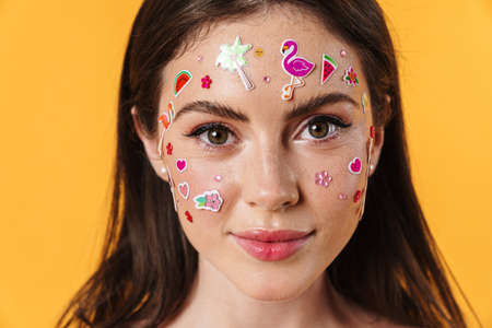 Image of young pleased woman with stickers on face looking at camera isolated over yellow backgroundの写真素材