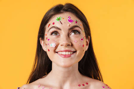 Image of young cheerful woman with stickers on face smiling at camera isolated over yellow backgroundの写真素材