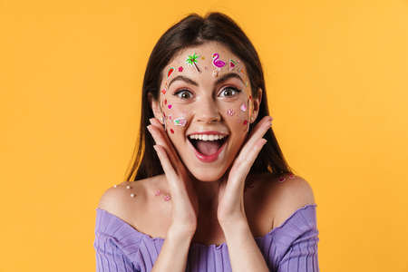 Image of delighted woman with stickers on face expressing surprise on camera isolated over yellow...