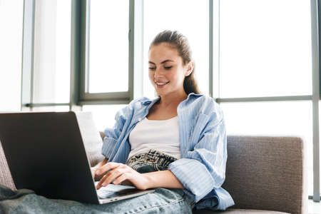 Image of a young happy smiling girl indoors at home using laptop computer