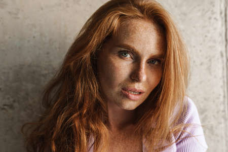 Image of redhead sensual woman looking at camera while posing near concrete wall at homeの写真素材