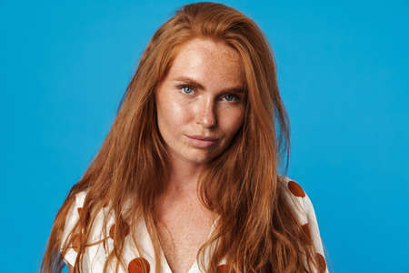 Portrait of a beautiful young woman with long red hair wearing summer clothes standing isolated over...