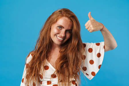 Portrait of a beautiful cheerful young woman with long red hair wearing summer clothes standing...