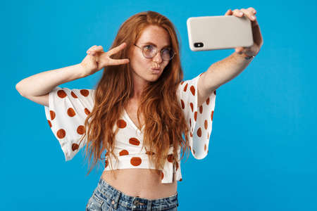 Portrait of a beautiful cheerful young woman with long red hair wearing summer clothes standing...