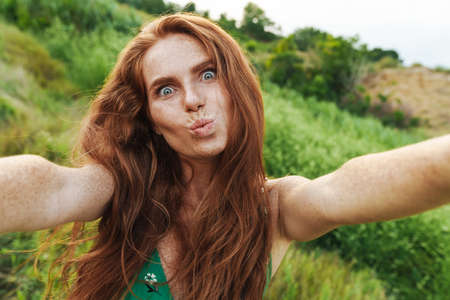 Young happy beautiful woman taking selfie while standing in the green filed