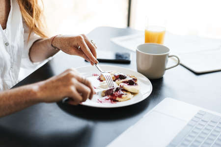 Cropped image of businesswoman having breakfast while working with laptop in kitchen at homeの写真素材
