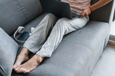 Cropped image of woman working with laptop while sitting on couch at homeの写真素材