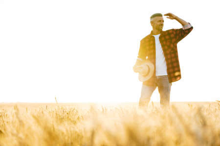 Image of pleased adult man with straw hat looking aside while standing at cereal fieldの写真素材