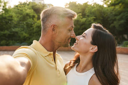 Portrait of romantic middle-aged couple man and woman taking selfie photo and hugging while walking...