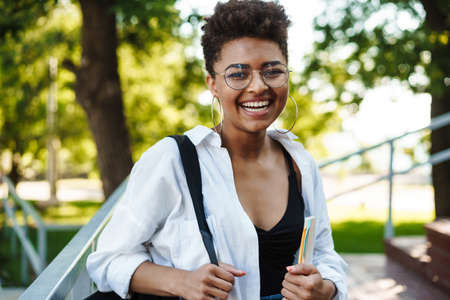 Attractive young african young student girl walking in the park, carrying textbooks