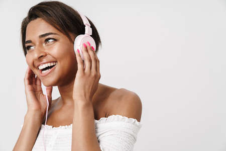 Image of joyful african american woman laughing and using headphones isolated over white background