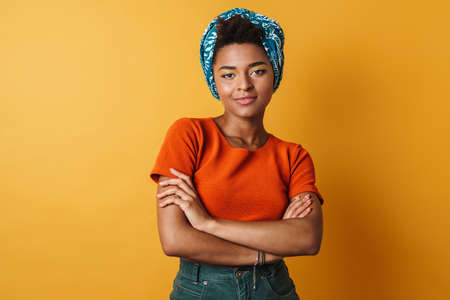 Image of pleased african american woman posing and looking at camera isolated yellow backgroundの写真素材