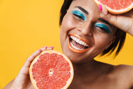 Image of shirtless african american woman laughing while posing with grapefruit isolated over yellow wallの写真素材