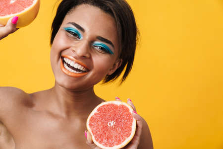 Image of shirtless african american woman holding grapefruit and smiling isolated over yellow wallの写真素材