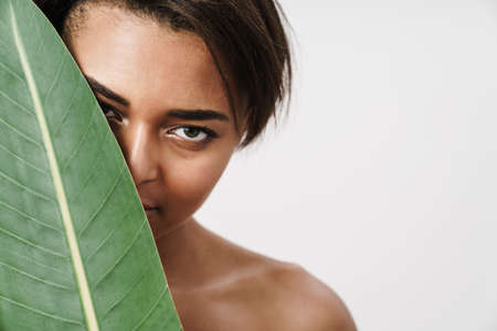 Image of shirtless african american woman posing with green leaf isolated over white background
