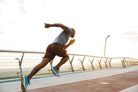 Side view of a young african man jogger exercising outdoors on a bridgeの写真素材