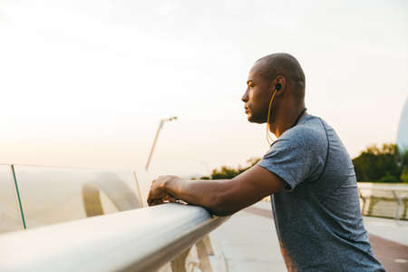 Relaxed african sportsman standing on the bridge, wearing headphonesの写真素材