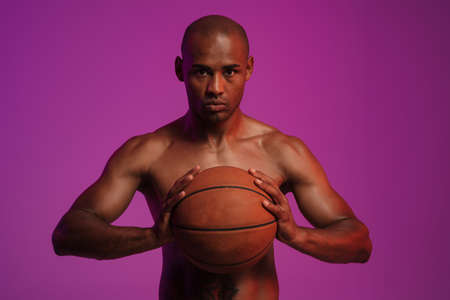 Image of a handsome concentrated strong african fitness sports man posing isolated over pink wall background while holding basketballの写真素材