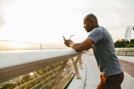 African american athlete man listening to the music and using mobile phone outdoors