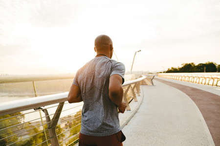 Side view of a young african man jogger exercising outdoors on a bridge