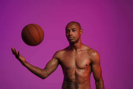 Photo of young handsome strong african fitness sports man posing isolated over pink wall background with basketballの写真素材