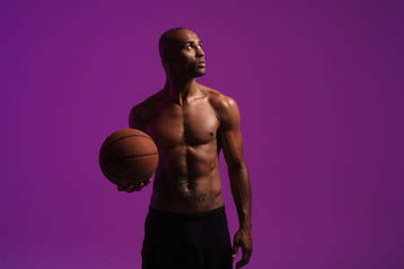 Picture of a concentrated strong african fitness sports man posing isolated over purple wall background while holding basketballの写真素材