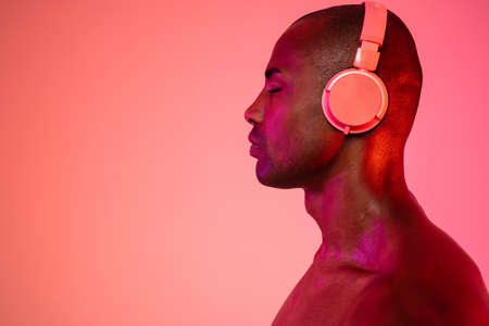 Side view photo of african concentrated man posing isolated over neon wall background while listening music with headphonesの写真素材