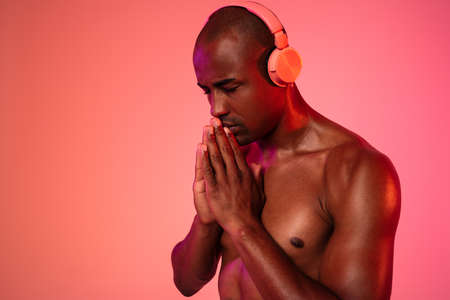 Image of african praying fitness man posing isolated over neon wall background while listening music...