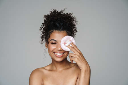 Image of shirtless african american woman smiling and using powder sponge isolated over grey wallの写真素材