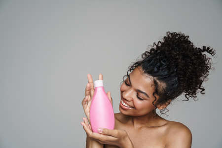 Image of shirtless african american woman smiling while posing with shampoo lotion isolated over...