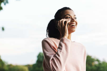 Image of happy african american girl talking on mobile phone while walking in summer parkの写真素材